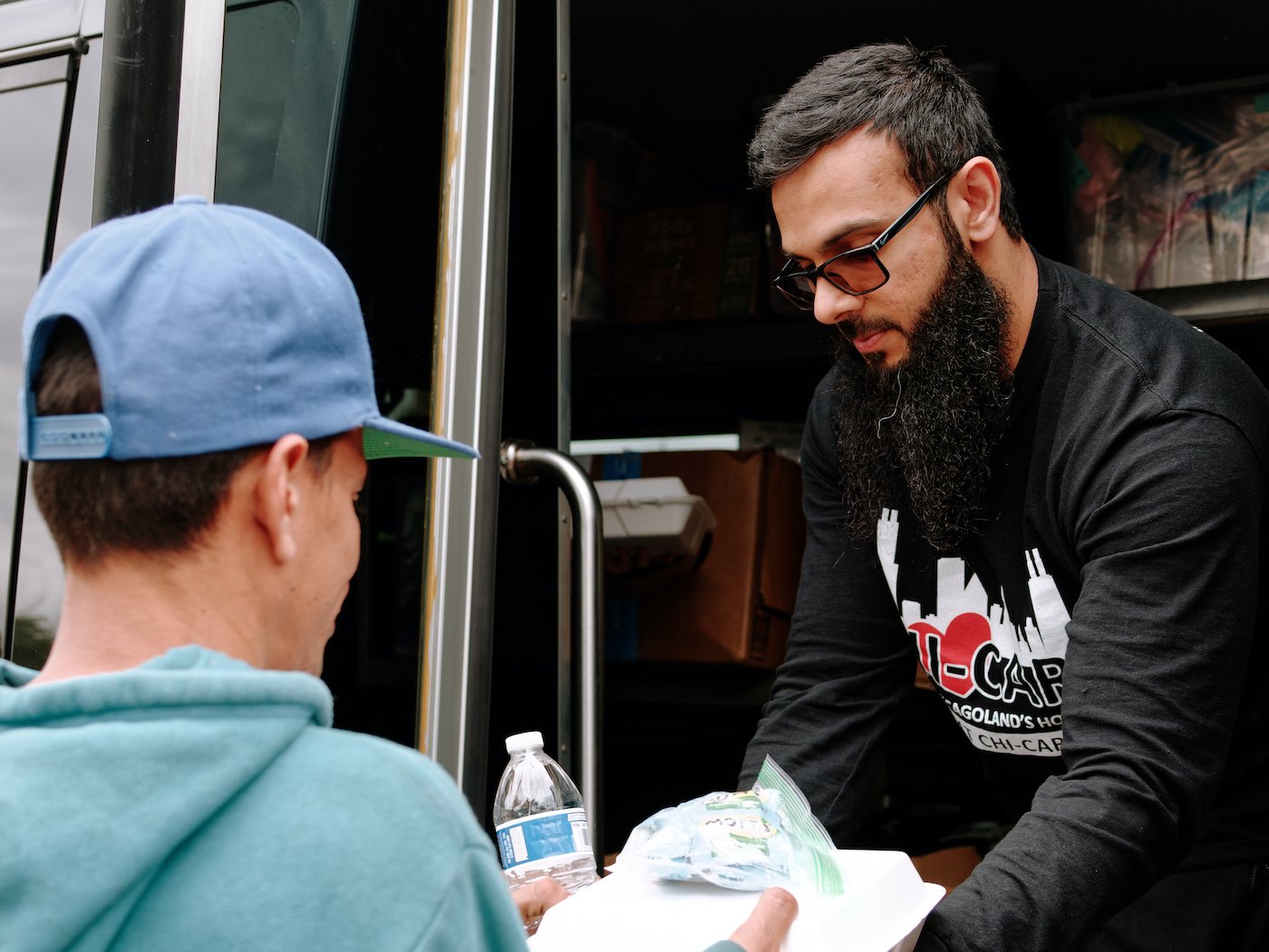 A man hand a meal and water bottle to a waiting man from a van