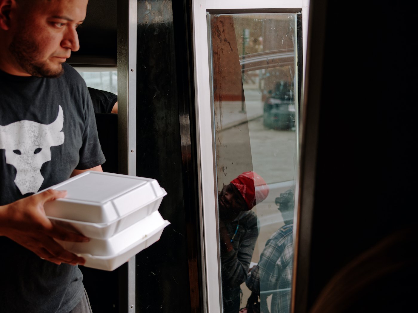 A man hands meals in styrofoam boxes out of a van door