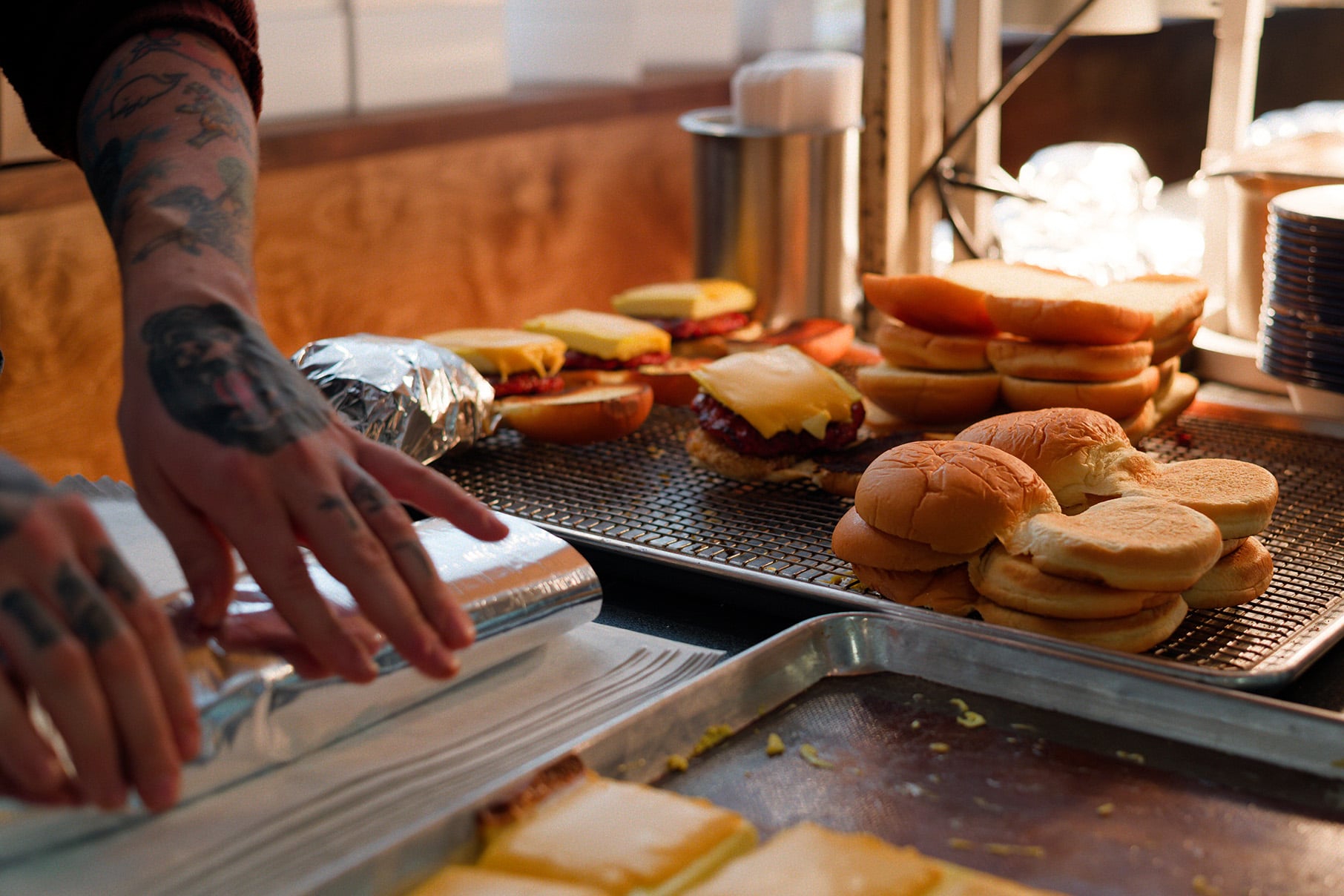 Hands wrap a sandwich in foil next to others awaiting assembly