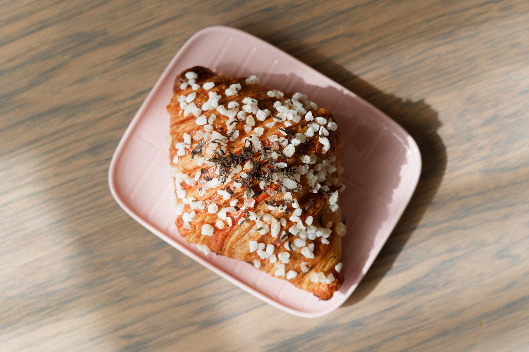 A croissant on a pink dish, topped with shaved truffle and sugar pearls