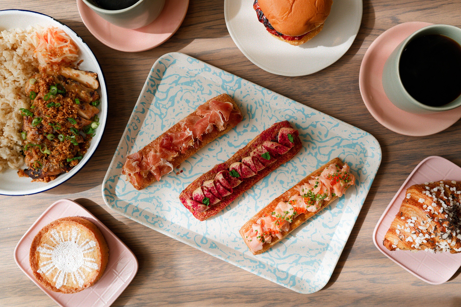 A platter of three Danish pastries surrounded by other plates of food seen on a table from overhead