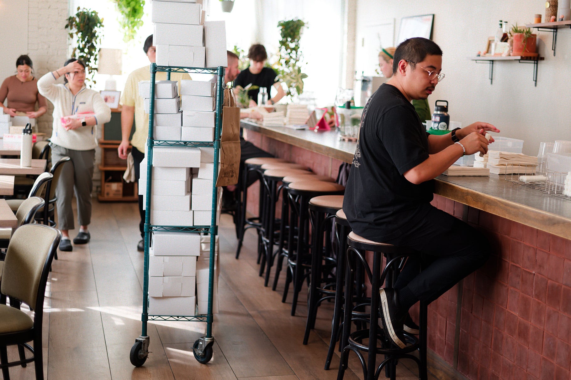 A cart of boxes stands in the middle of a restaurant as staff work around it
