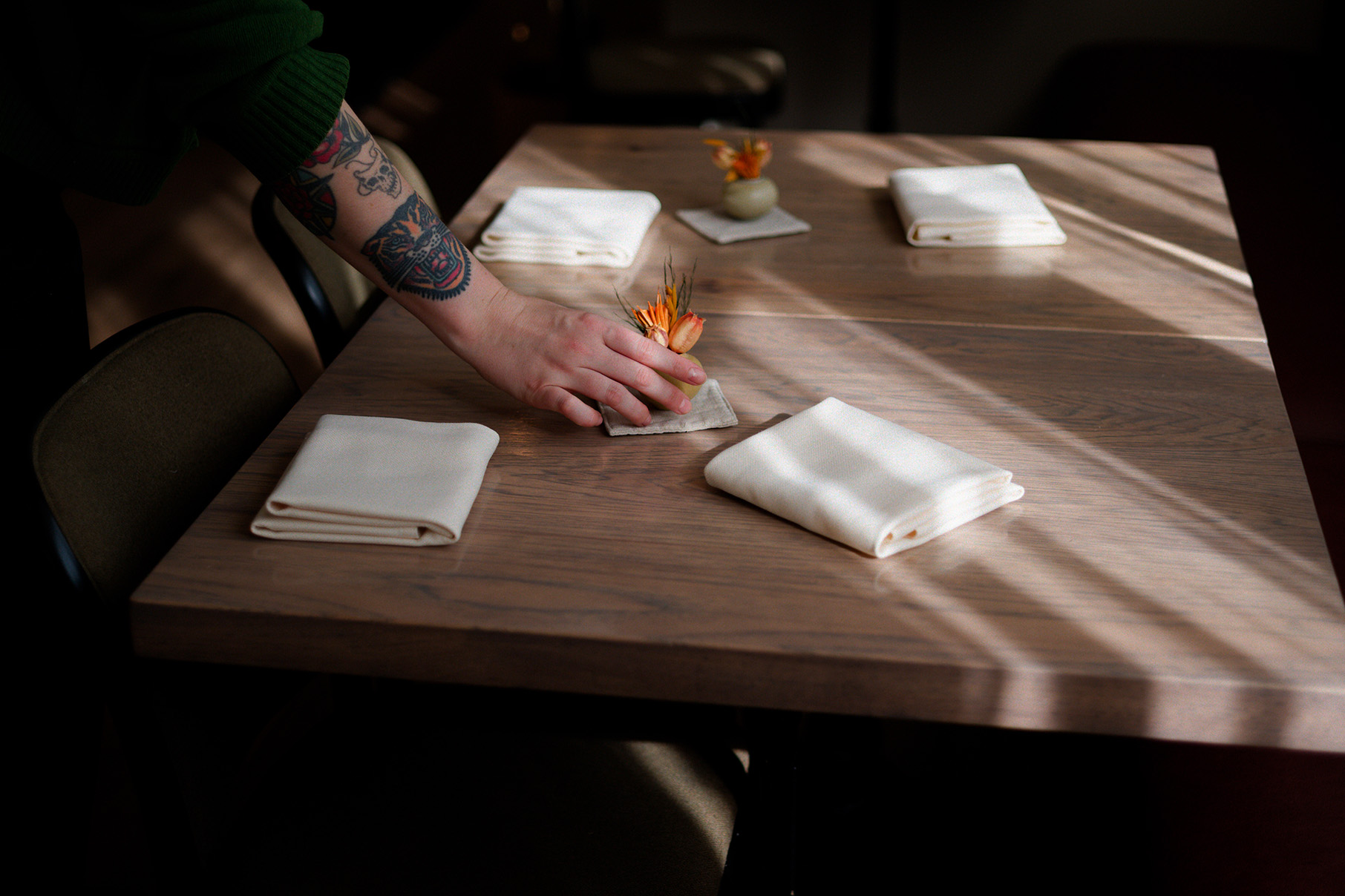 A hand places a small vase with flowers on a table with napkins and other vases