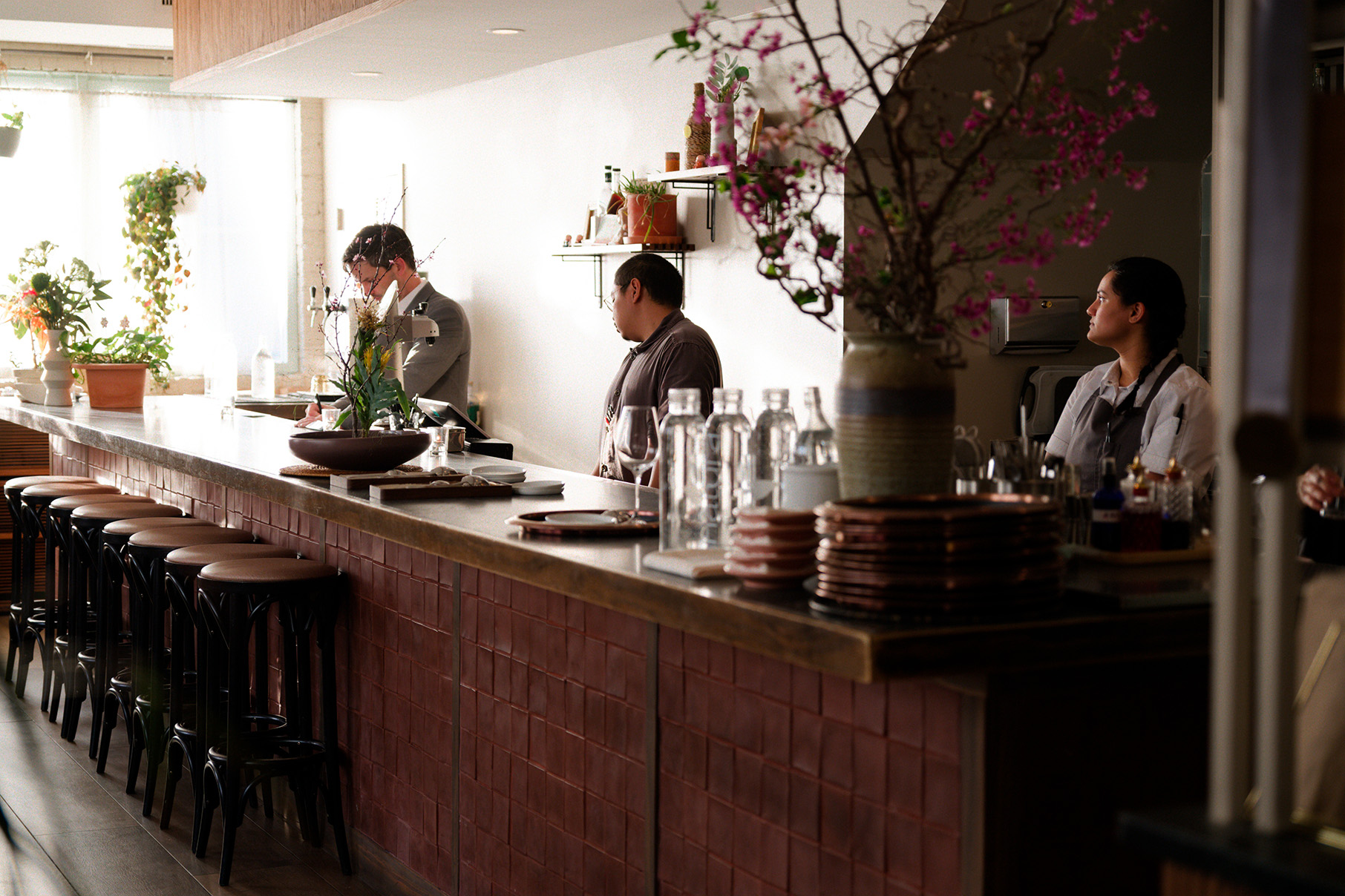 Three staff behind the bar at Kasama, which has floral arrangements on it