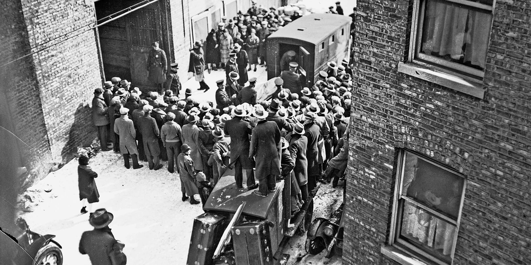A crowd gathers outside the garage while the body of a victim of the St. Valentine's Day Massacre is removed.