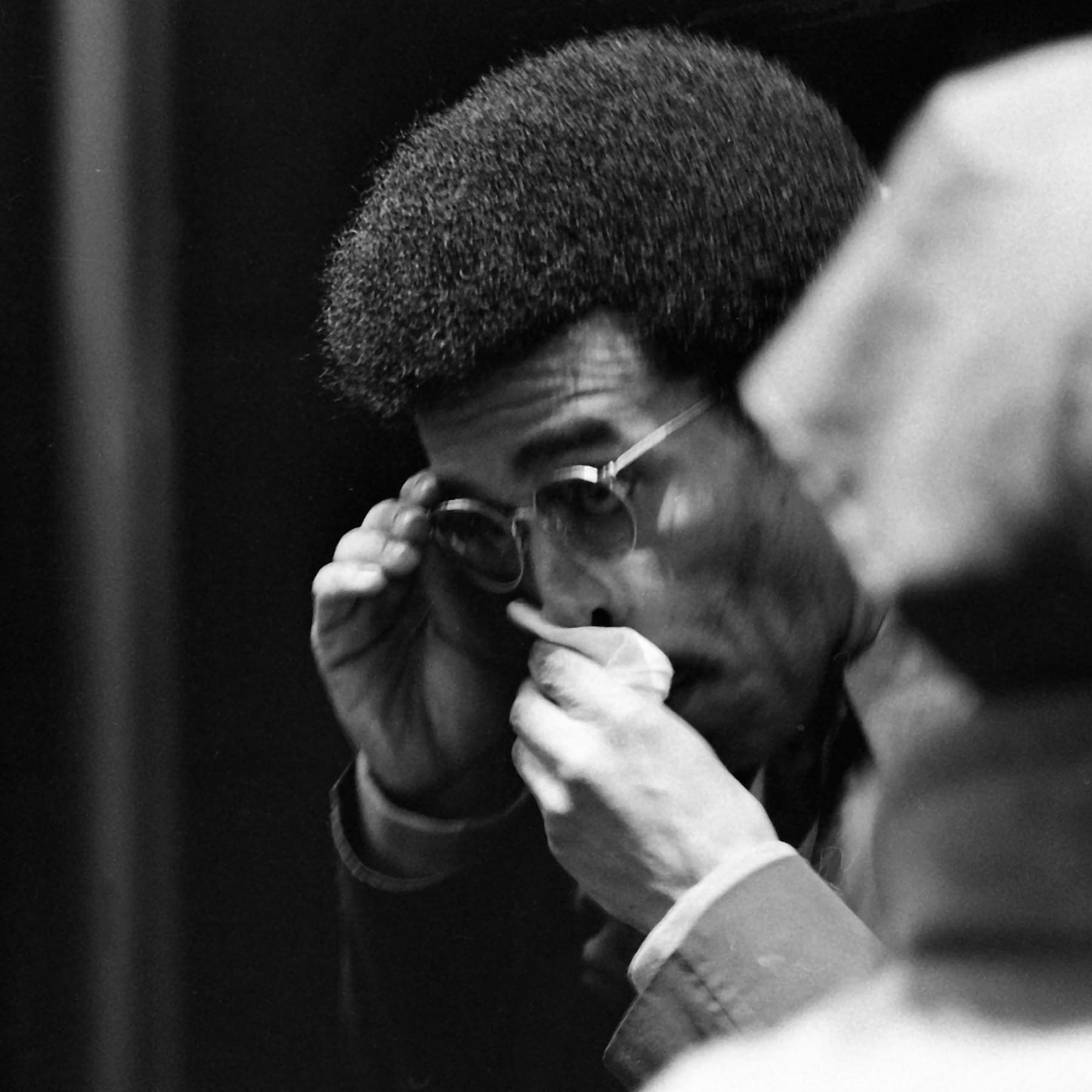 A black and white photo of a person adjusting their glasses, wiping away tears.