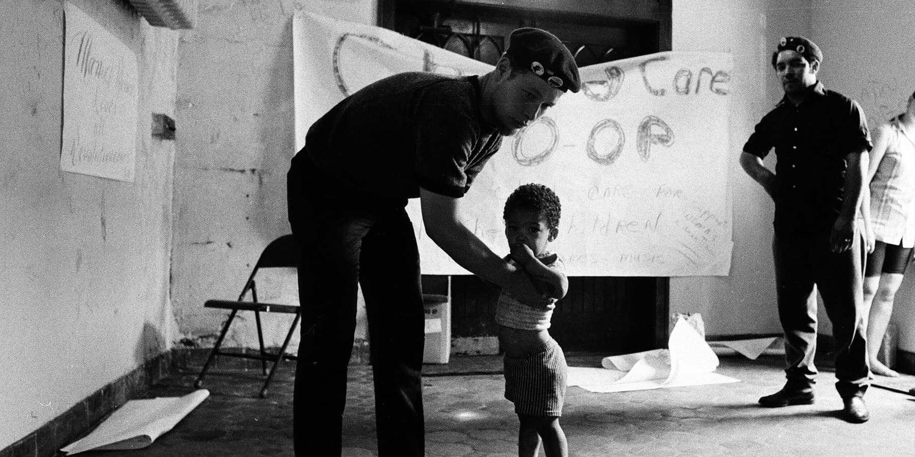 Jiménez reaching for a child in front of a sign reading Child Care Co-Op