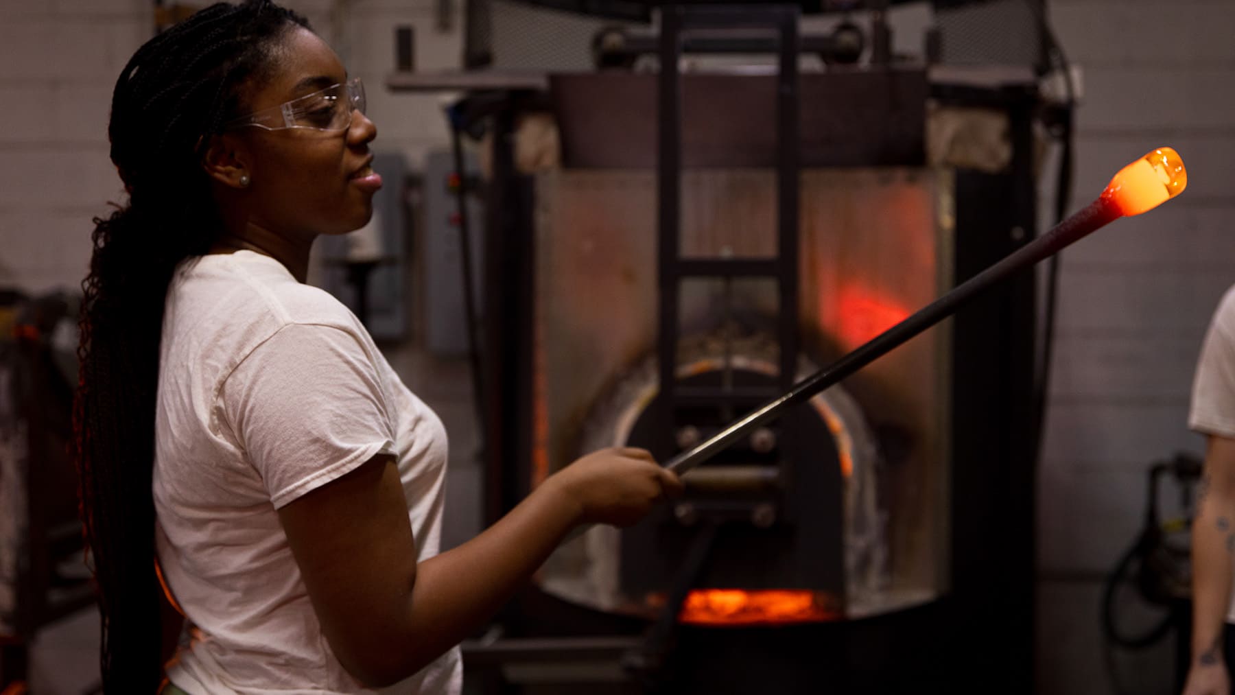 Glassblower Nae-Nae McGee rolls molten glass attached to a rod.