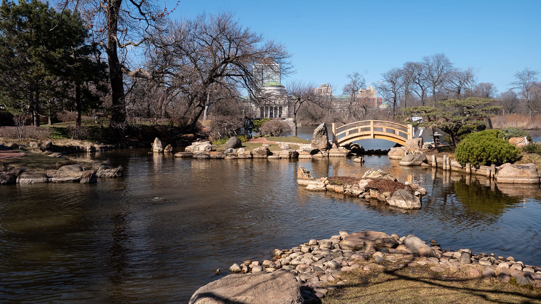 A small arched wooden bridge spans over water to a small island.