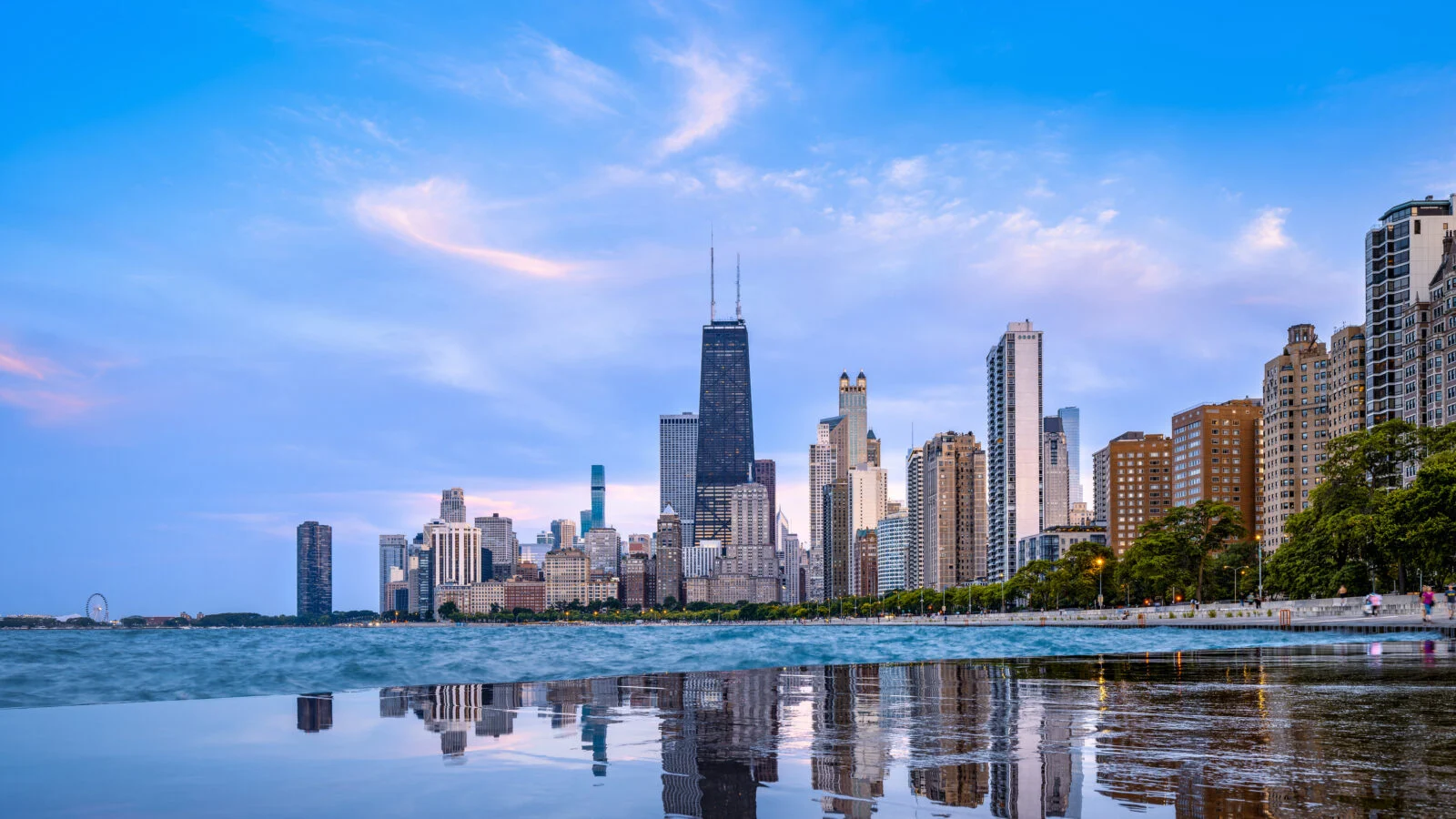 Lake Michigan and wet pavement reflecting the Chicago skyline and wispy clouds in the background.