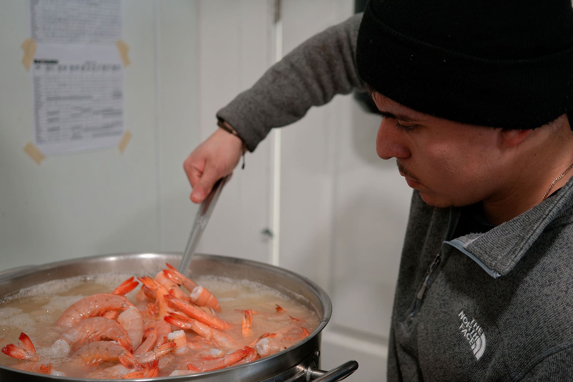 A worker stirs a large pot of boiling shrimp.