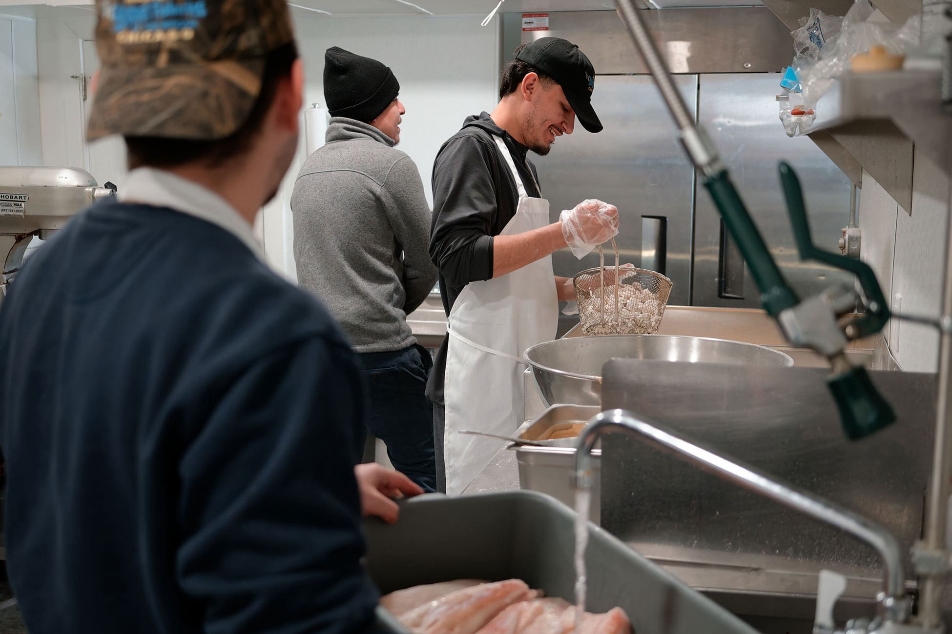 Employees stand by work stations preparing fish in a pan and a basket of shrimp for frying.