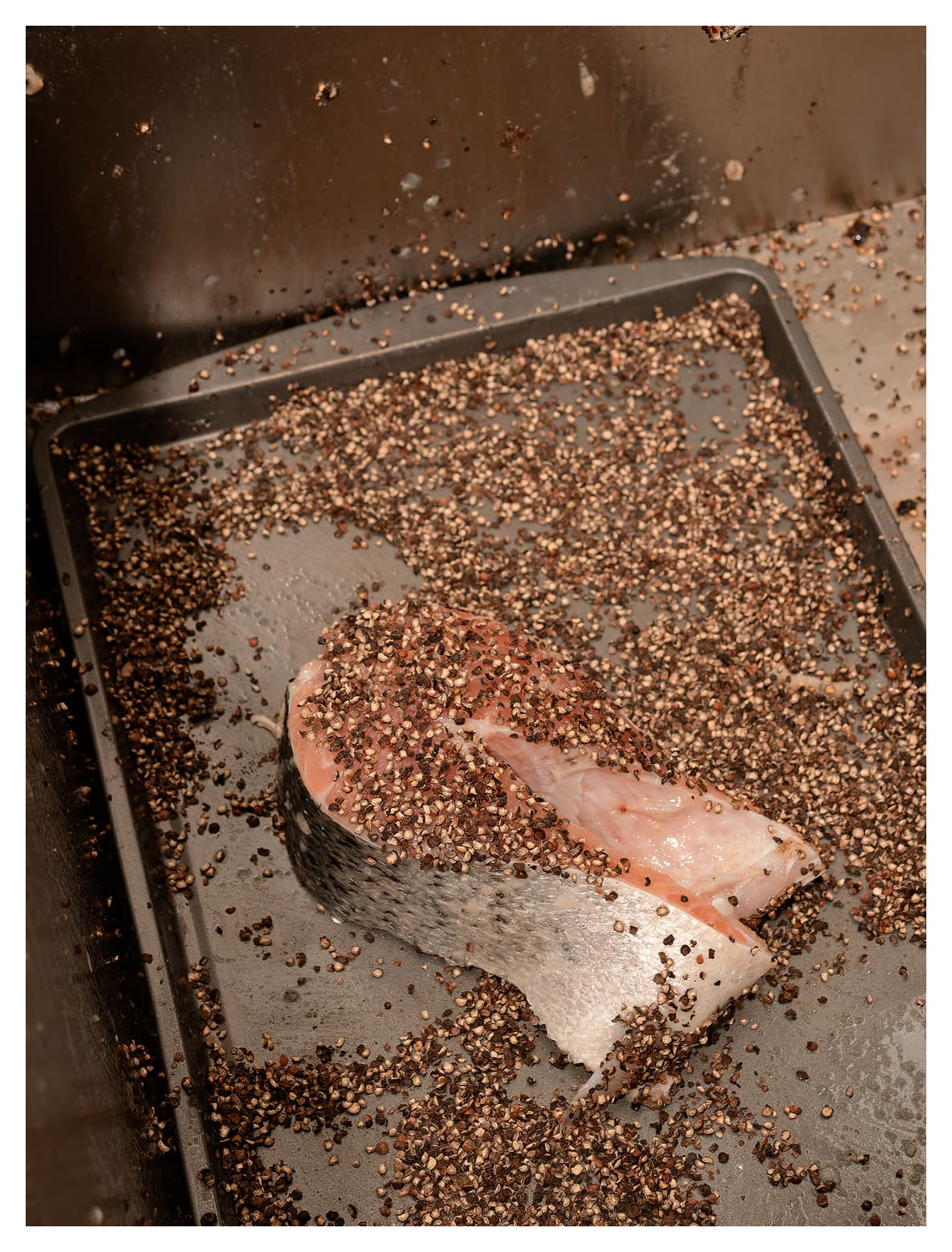 A piece of fish rests on a cooking sheet covered with spices