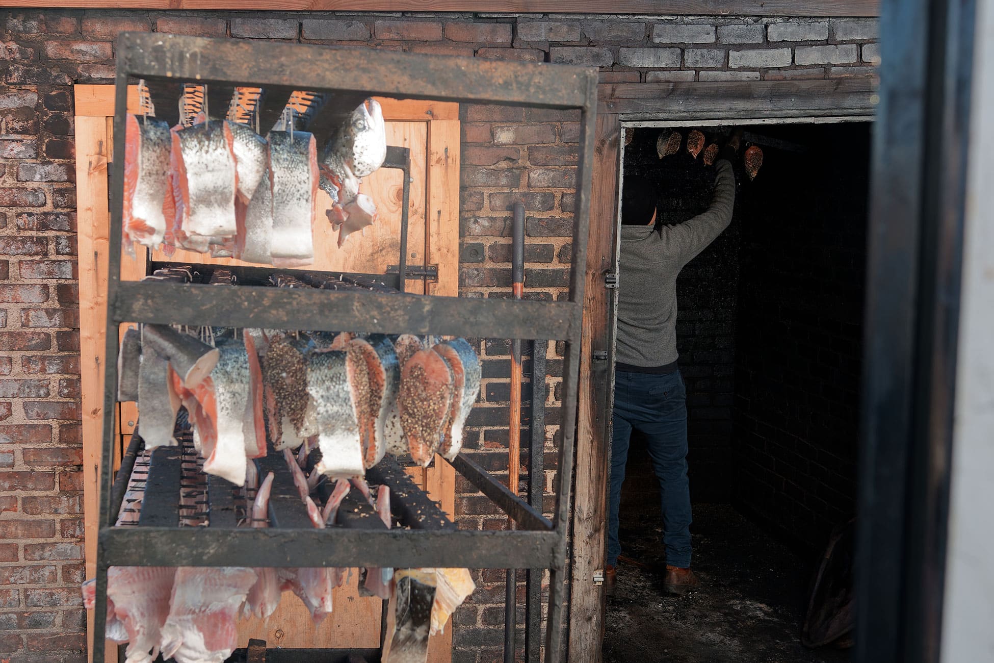 A rack of fish waits outside the smoke house as a worker hangs fish inside.