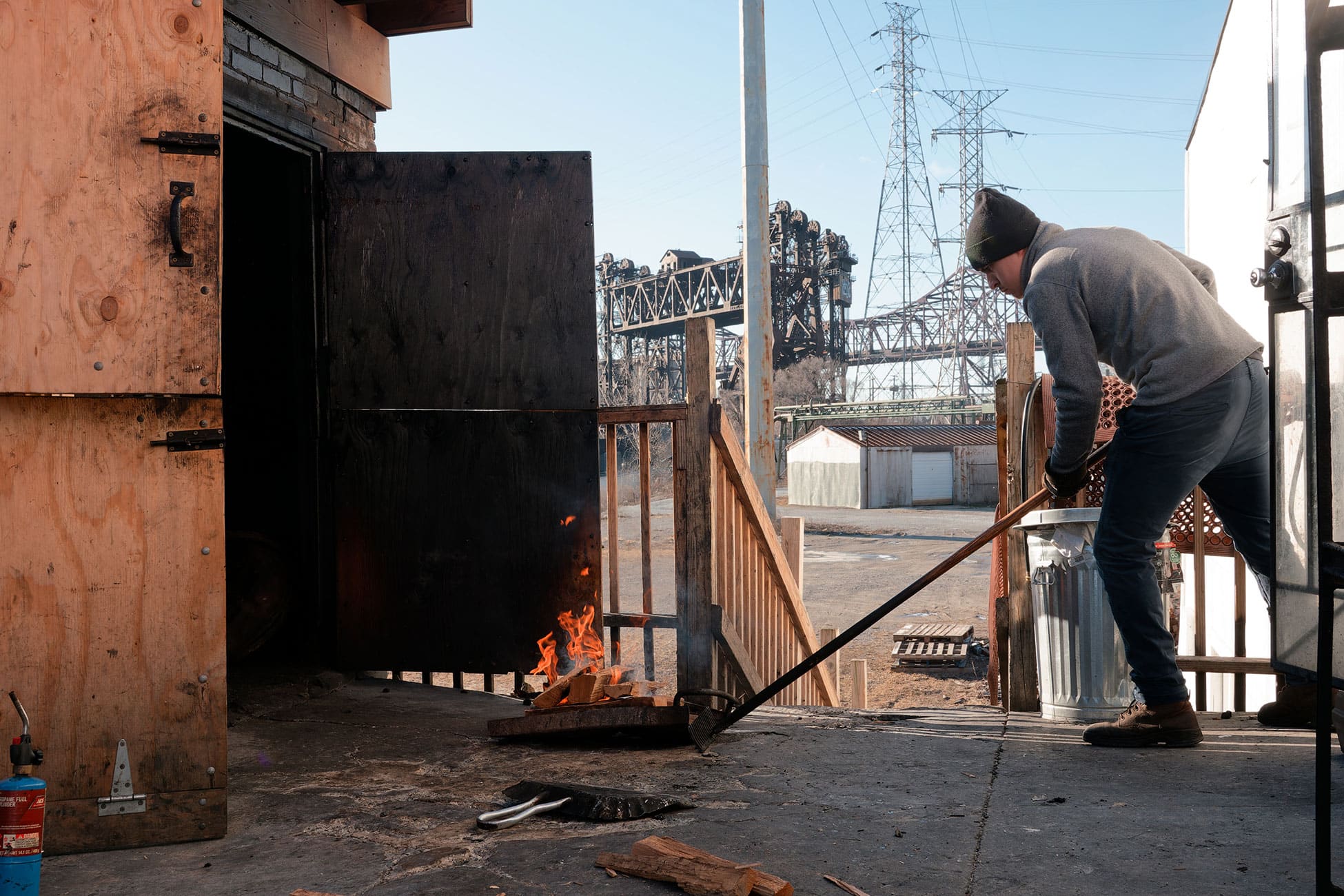 A worker pushes flaming logs into the smokehouse.