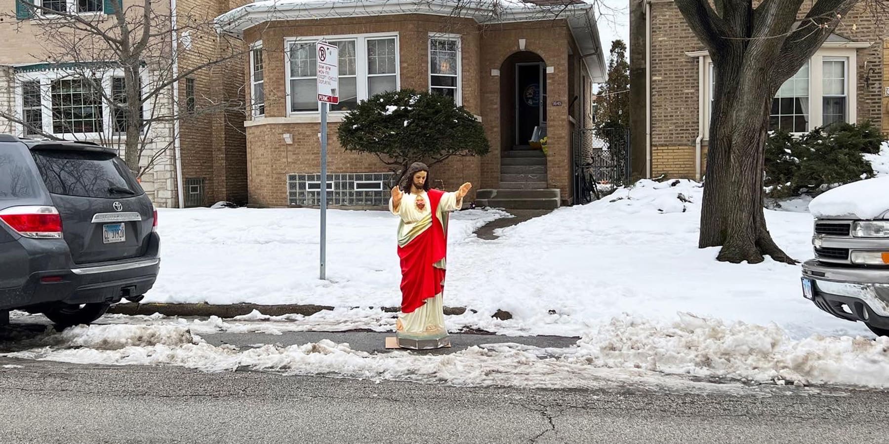 A four foot tall plastic Jesus decoration stands with arms raised claiming 'dibs' on a shoveled parking spot.