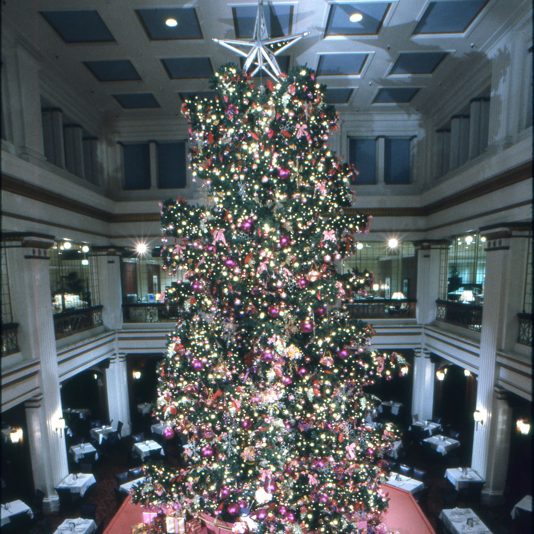A large Christmas tree adorned with decorations stands prominently in a spacious room filled with festive ambiance.