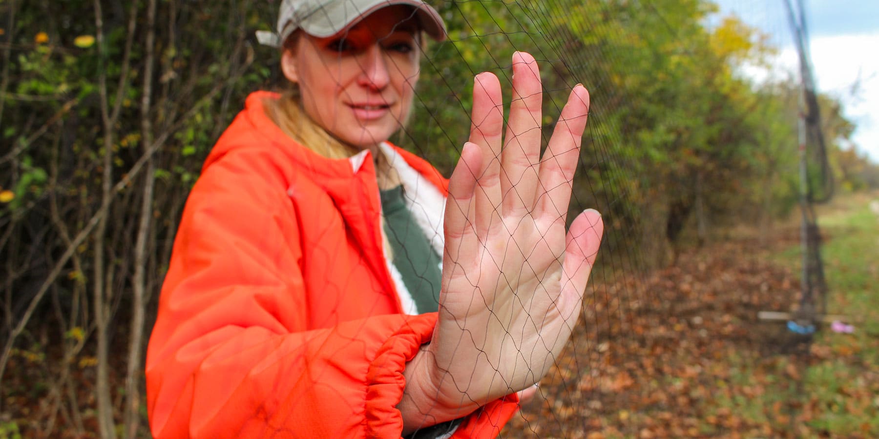 A woman holds up her hand against the bird net