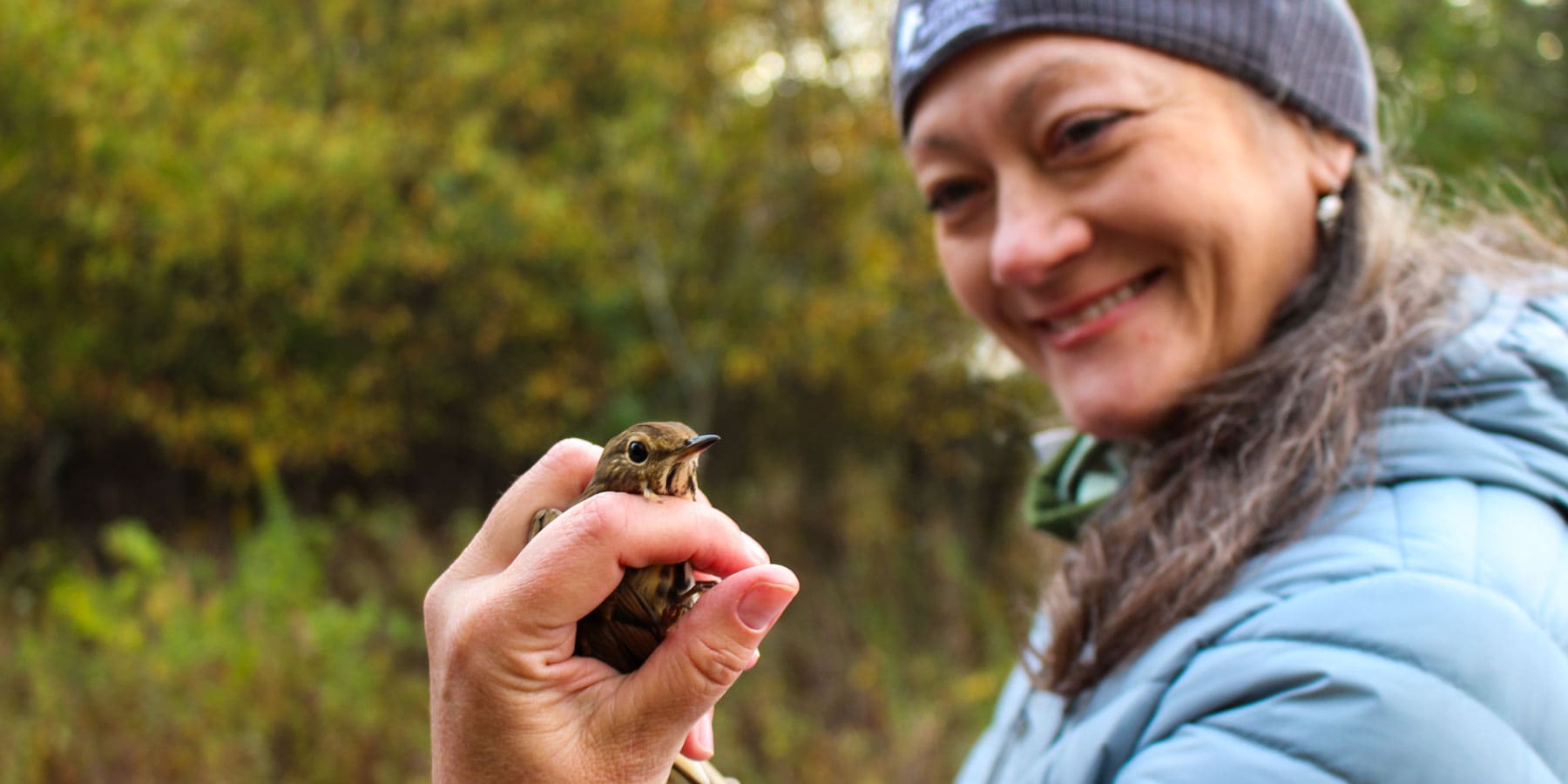 A worker smiles as she looks at the small bird in her hand