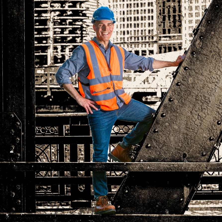 Host Geoffrey Baer stands on the beams of a bridge