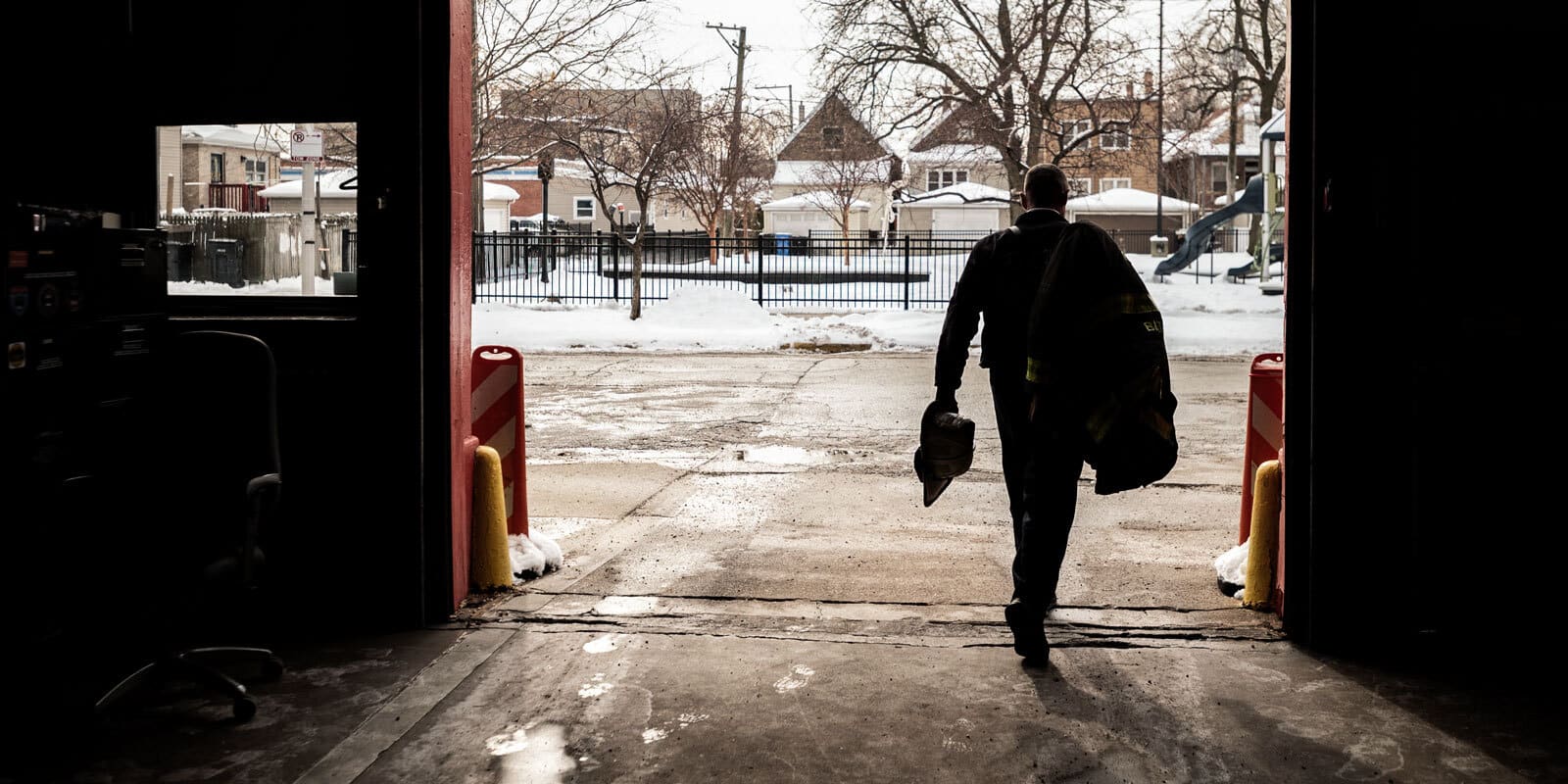A silhouetted fireman walks out of the station via the garage door