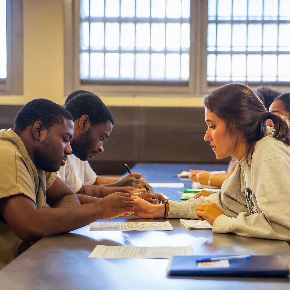 Woman helps prisoners at a table fill out forms