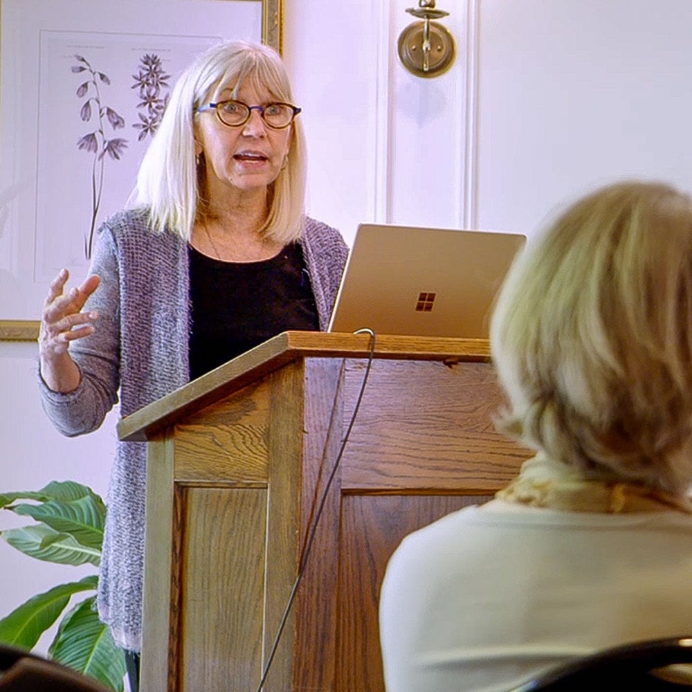 Maryanne at lectern speaking with a presentation