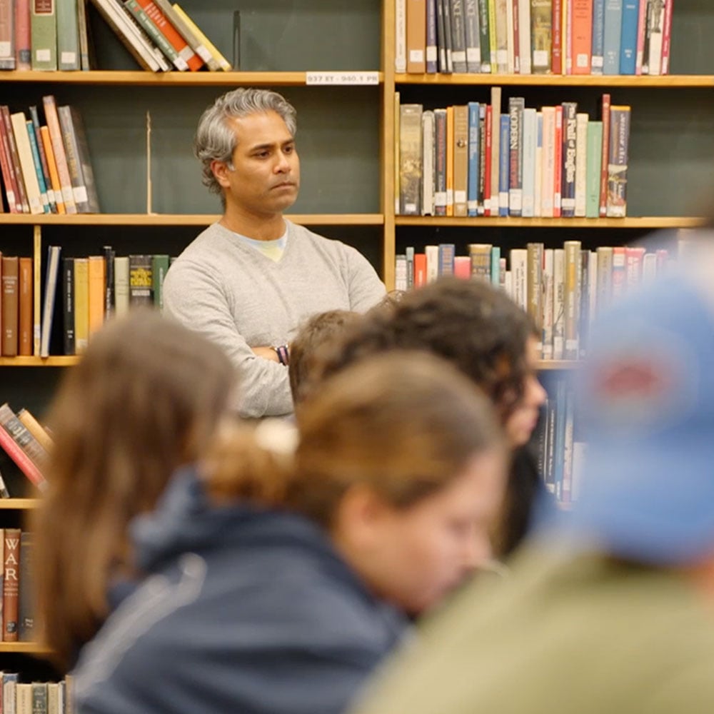 Miten next to bookshelves watching a proceeding