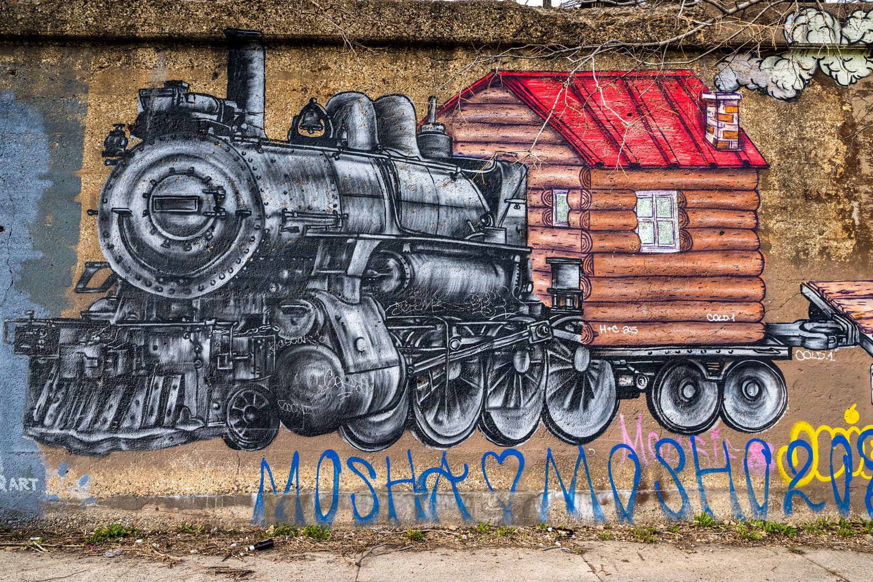A vibrant mural depicts a vintage steam locomotive attached to a wooden cabin on wheels. Graffiti below reads 