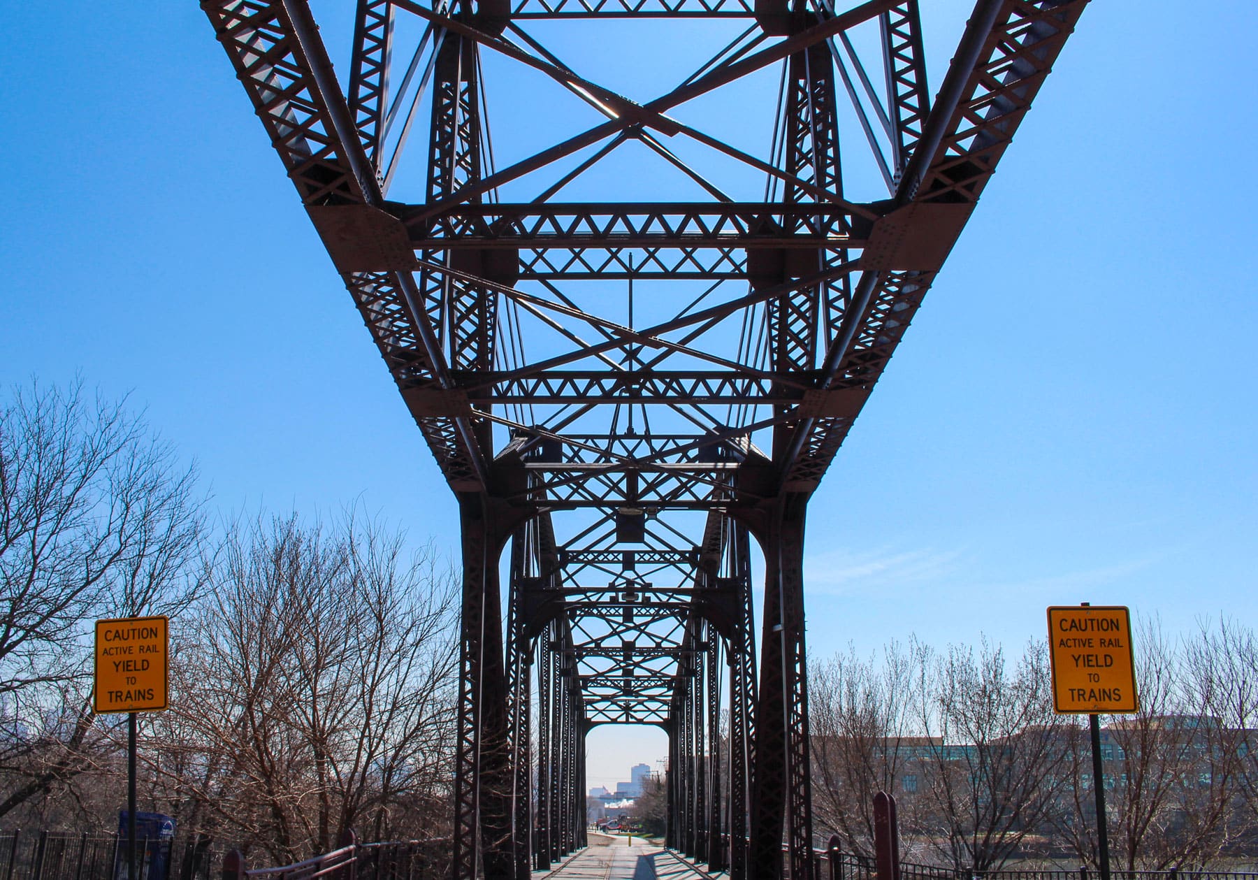 Looking down the path of an old bridge against a clear blue sky and bare trees.