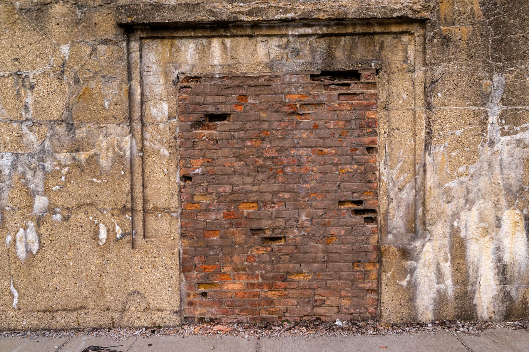 Old brick wall filling a former doorway in a textured concrete structure; the bricks are unevenly placed, adding a sense of historical decay.
