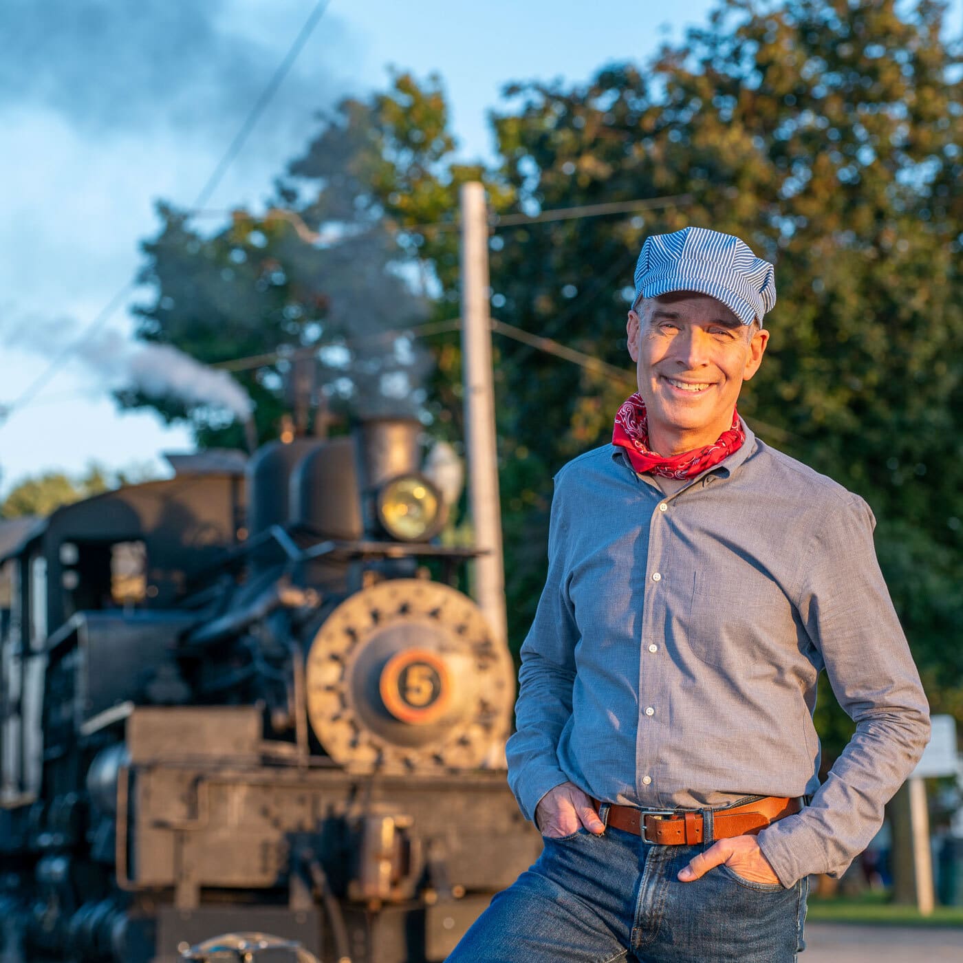 Host Geoffrey Baer stands in front of a steam engine