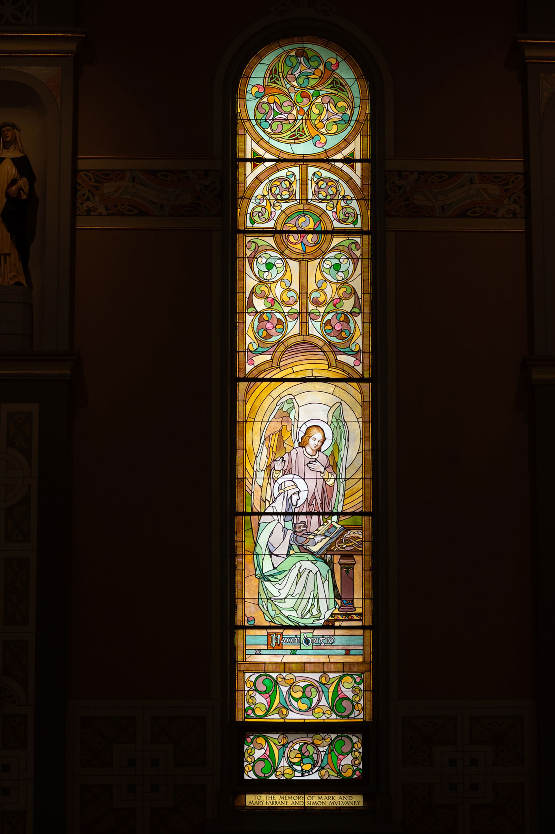 Stained glass window in Old St. Patrick's Church in Chicago depicting an angel instructing a seated saint, framed by O'Shaughnessy’s signature pastel Celtic interlace and geometric patterns.