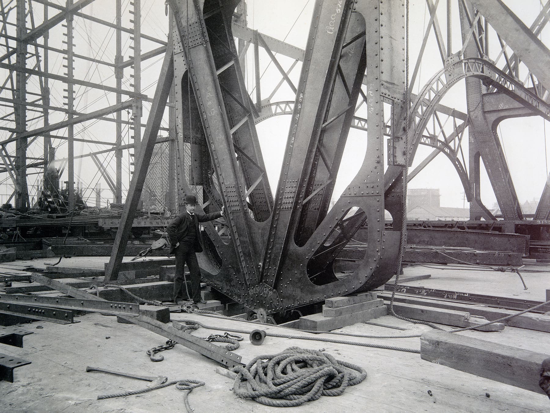 A worker stands next to a steel beam during construction of the Manufactures and Liberal Arts Building.