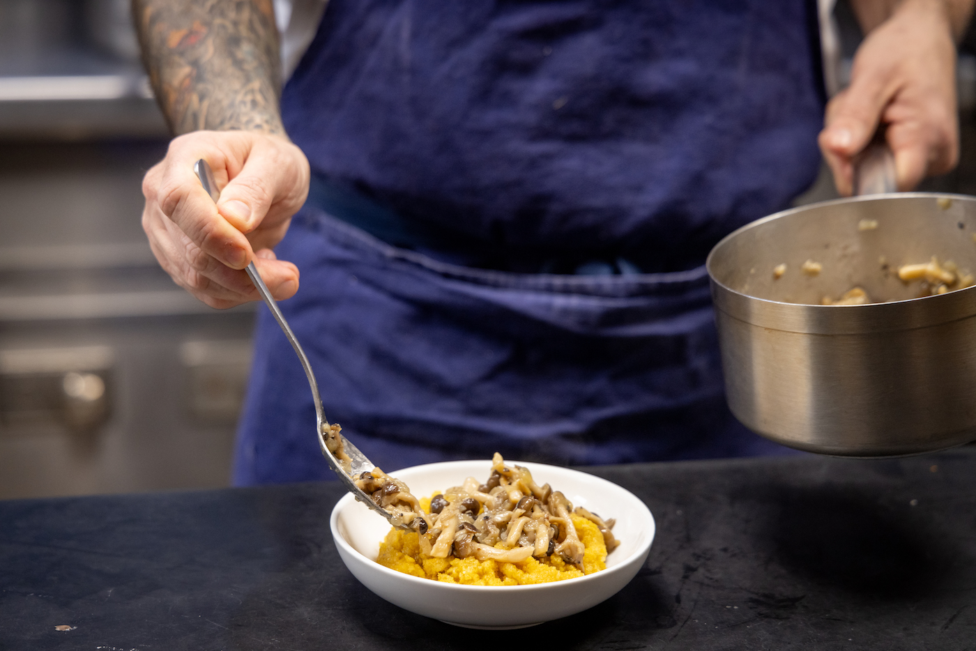 A hand spoons mushrooms on top of banosh, a Ukrainian grit
