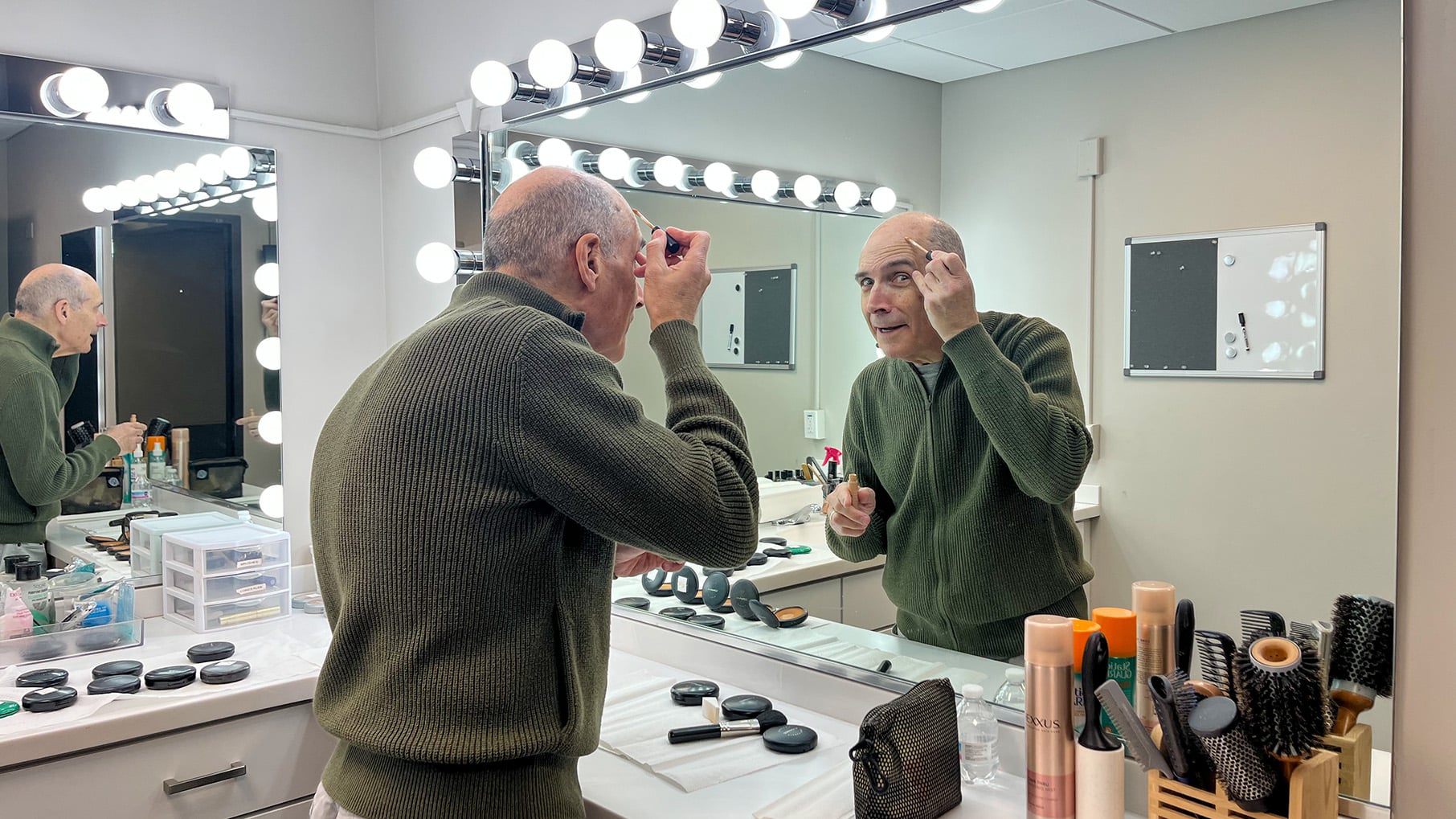 Geoffrey Baer puts on make-up in a brightly-lit make-up room