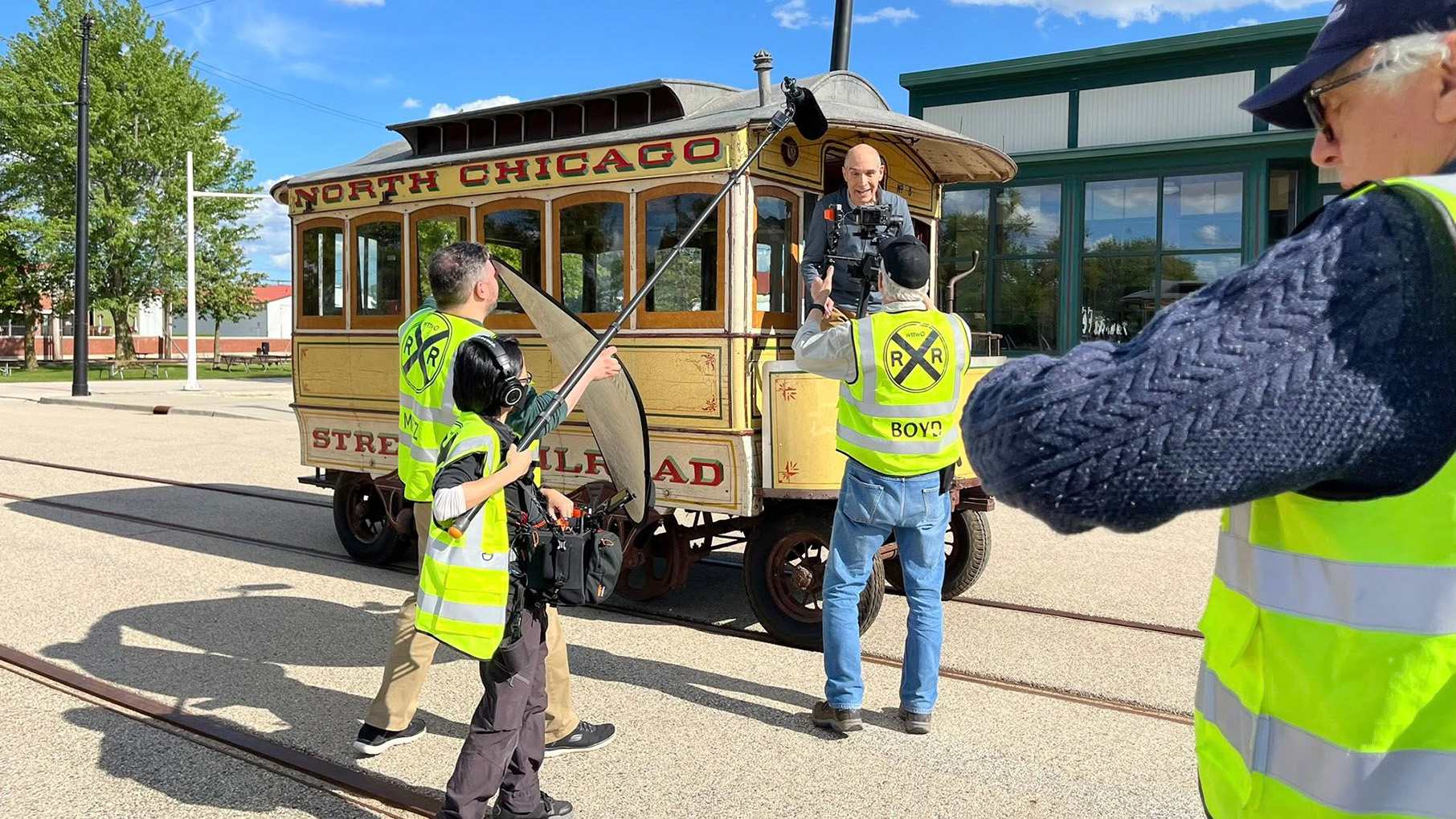 Geoffrey Baer aboard a horse-drawn, wooden streetcar while a crew films him