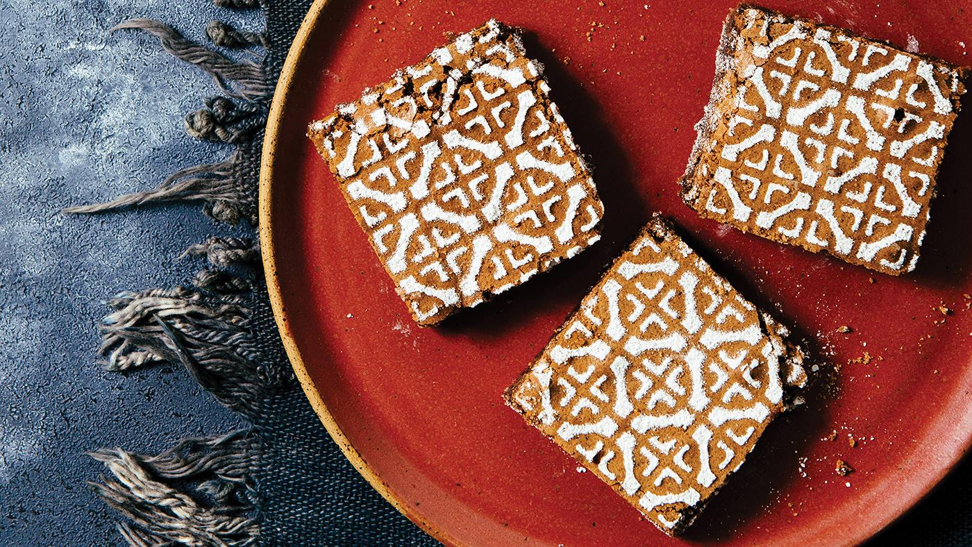 Three brownies with an intricate powdered sugar design sprinkled on top, sitting on a red plate