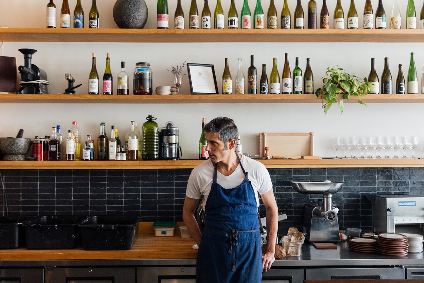 Ethan Pikas stands in front of a counter and shelves full of bottles and looks to the side