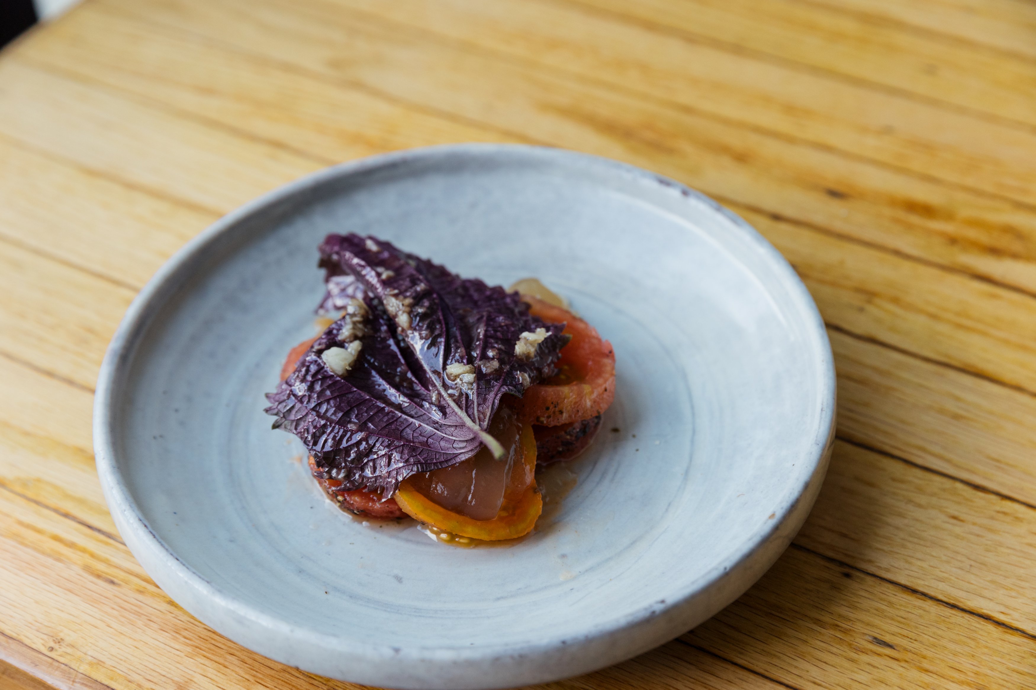 A plate with tomatoes topped with a purple shiso leaf