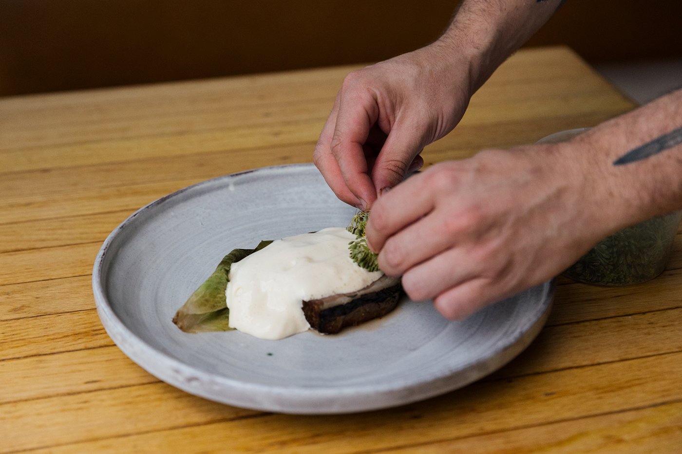 Hands put dill flowers on a sabayon on top of a short rib and chicory on a plate