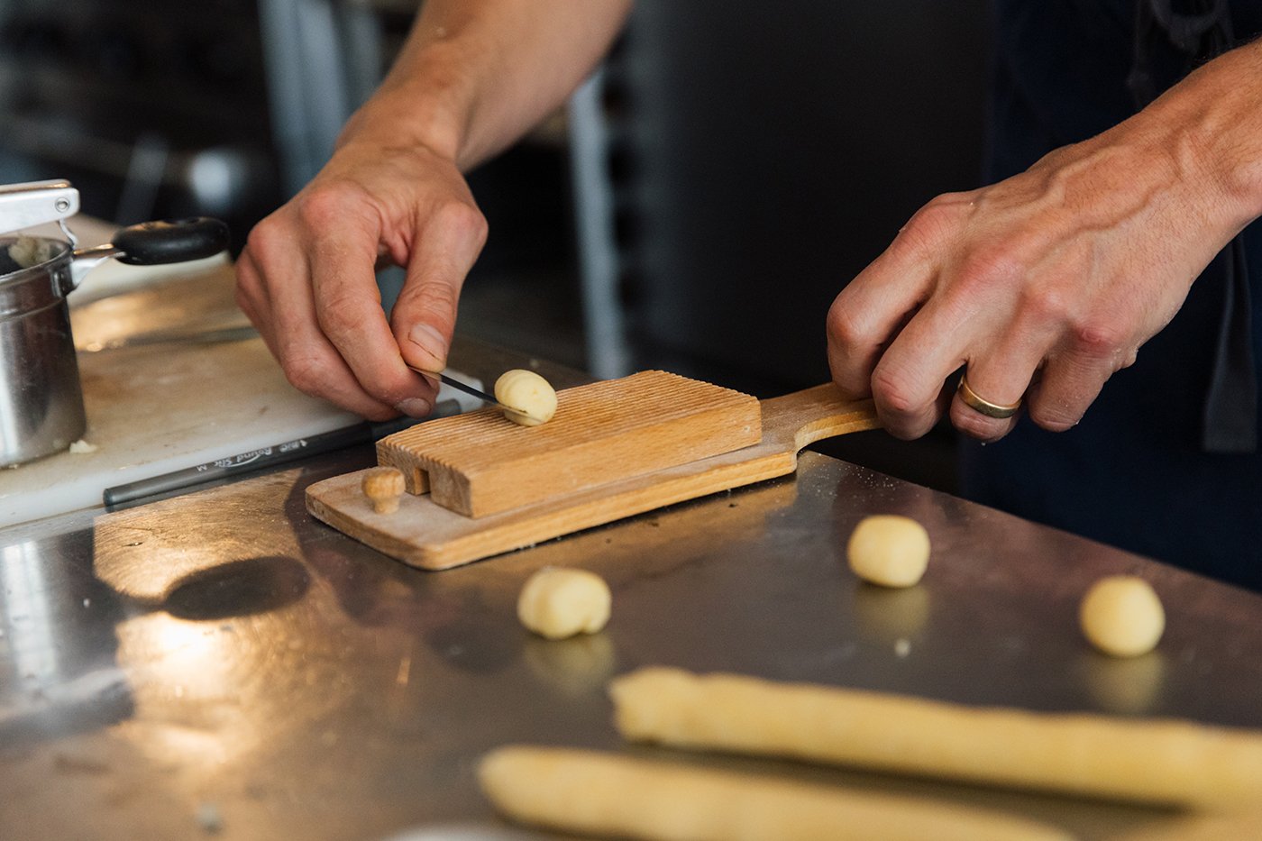A hand rolls a gnocchi on a wooden board