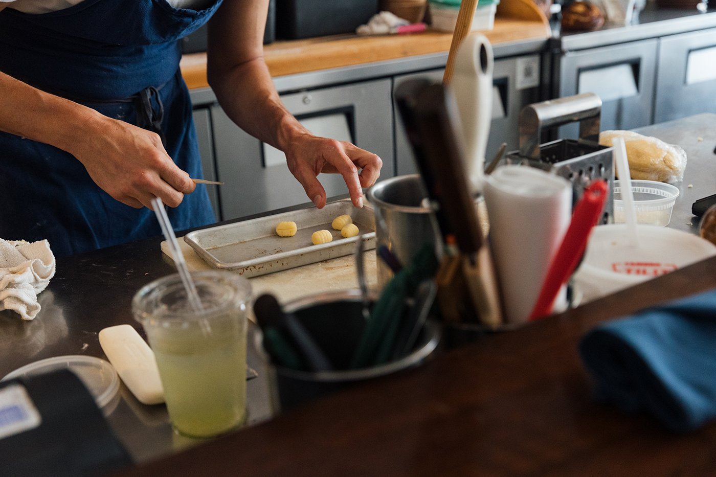Hands adjust four gnocchi on a sheet pan on a restaurant kitchen counter
