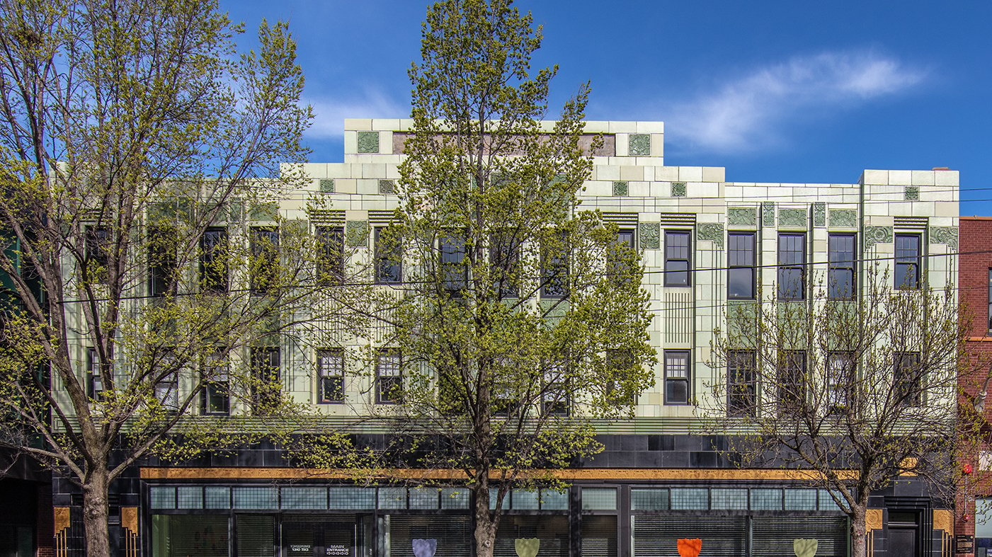 The green and white facade of the Chicago Bee branch of the Chicago Public Library behind trees