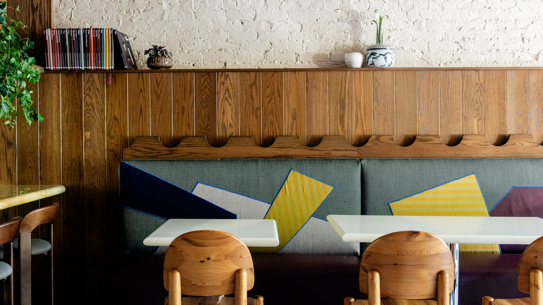 A couple chairs and tables against a wood and brick wall with colorfully patterned banquettes