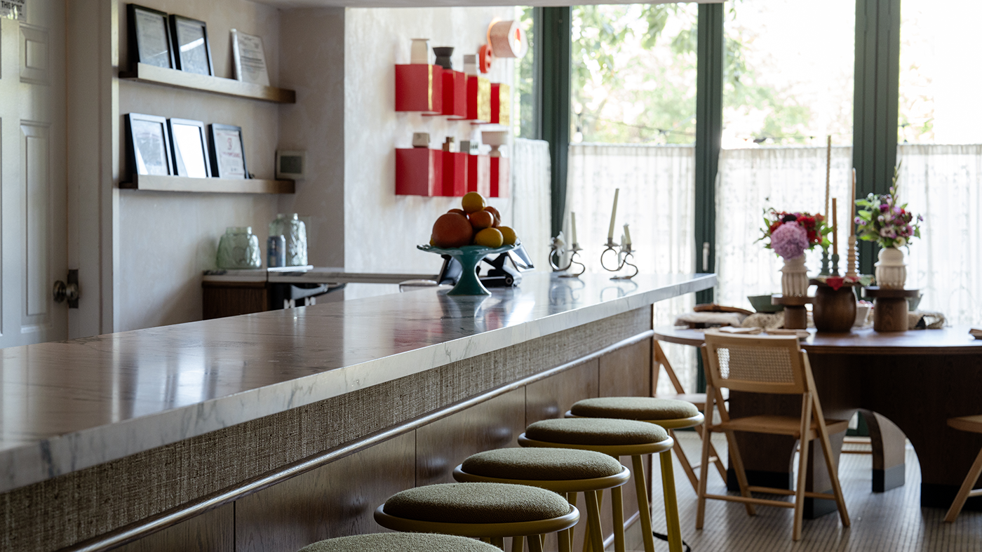 Bar stools in front of a bar with a table in the background in front of windows