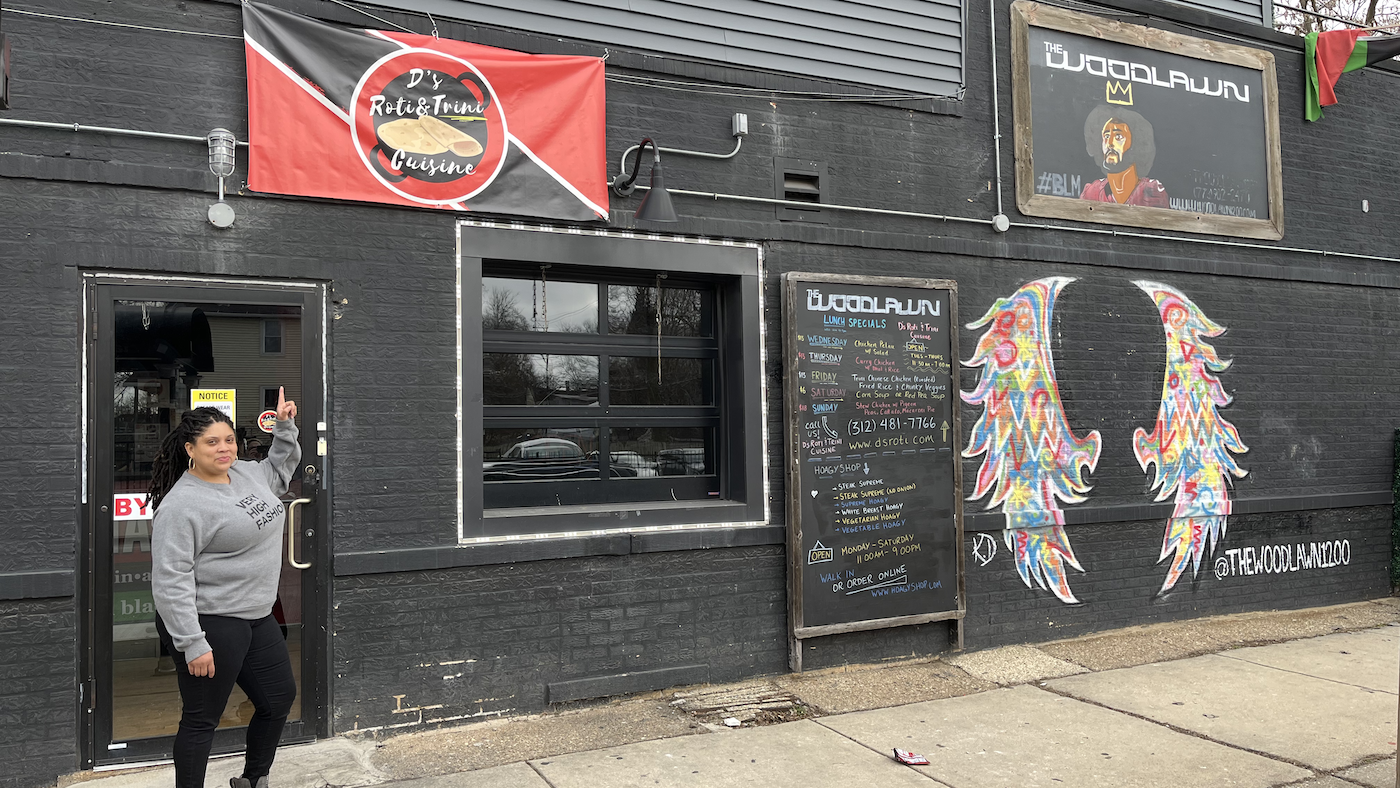 Dawn Lewis stands in front of the door of D's Roti in Chicago and points up at a sign with the restaurant's name