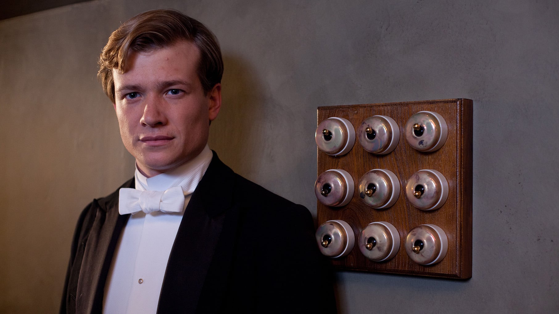 Jimmy Kent smiles in a tuxedo near a wall of switches