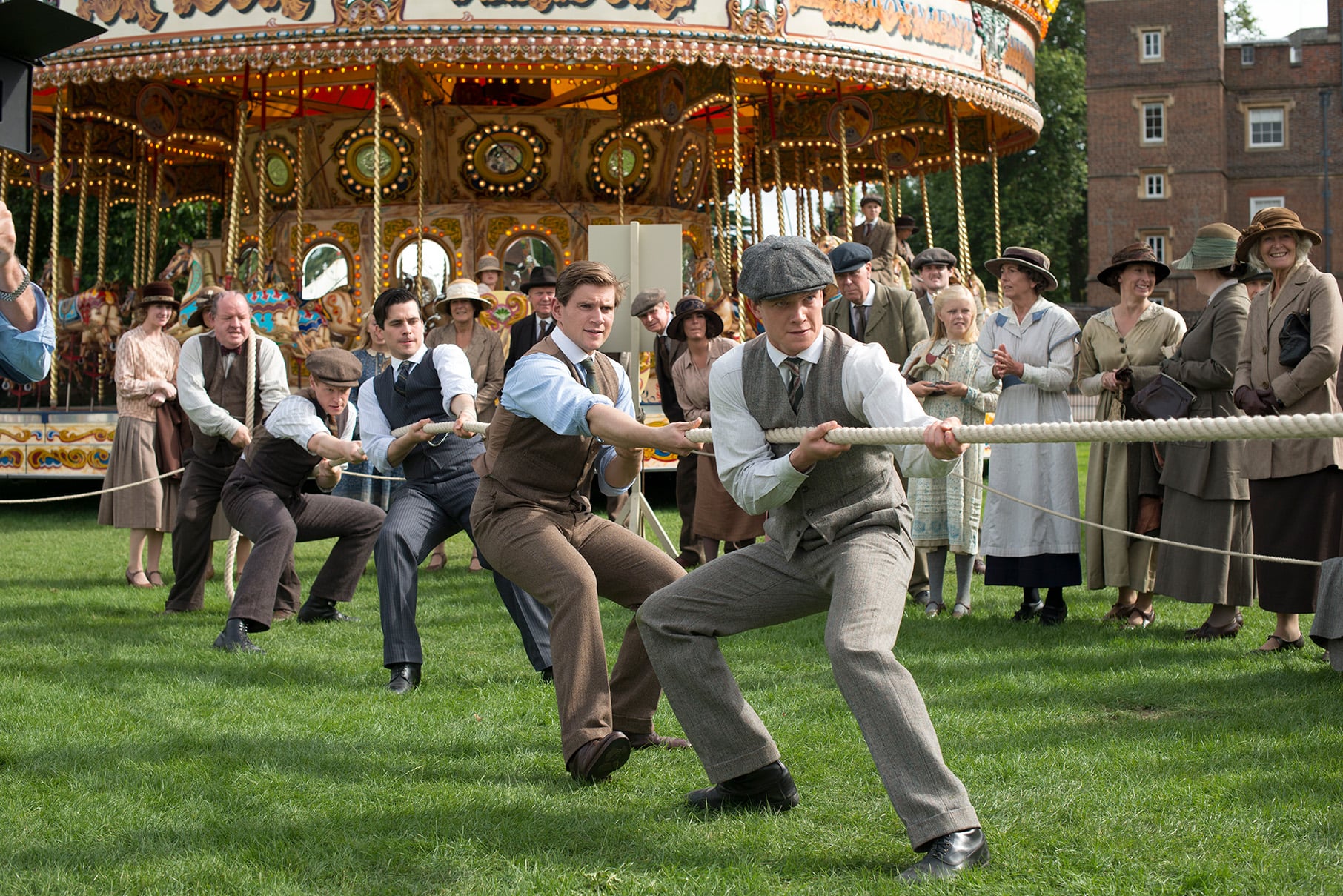 Men pull on a rope in tug of war in front of a crowd and a carousel
