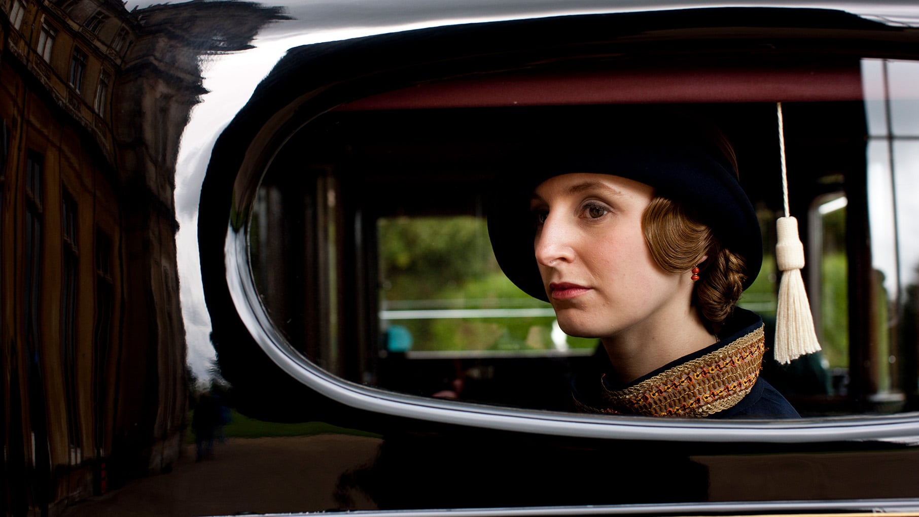 Edith in a hat is seen looking serious through a car window